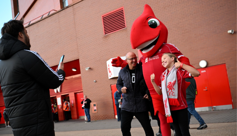 Two people getting their photo taken with the Liverpool Football Club mascot.