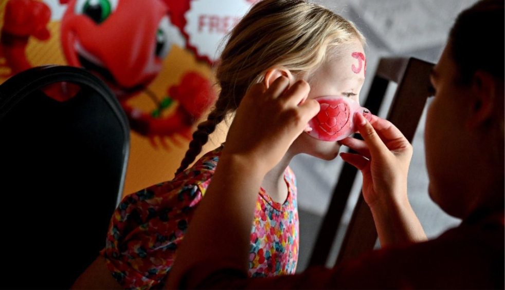 A young child getting her face painted with red colour.
