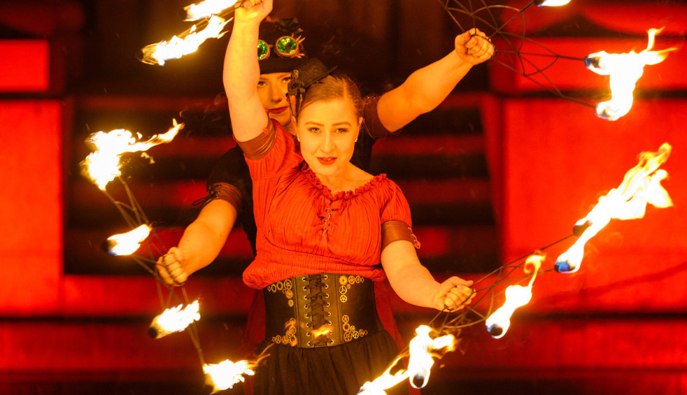 A woman holding several sticks with fire on the end, wearing a red top and a black belt.
