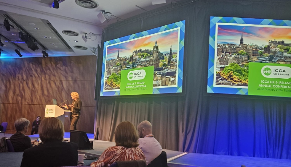 People sitting down listening to someone present on stage.