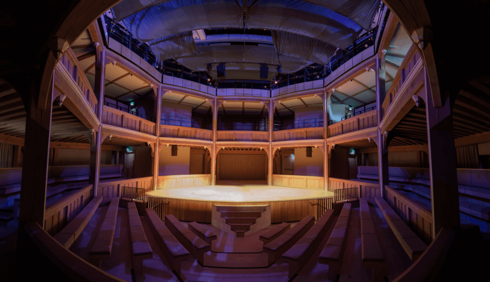 Inside of a theatre with the seats and stage made of wood.