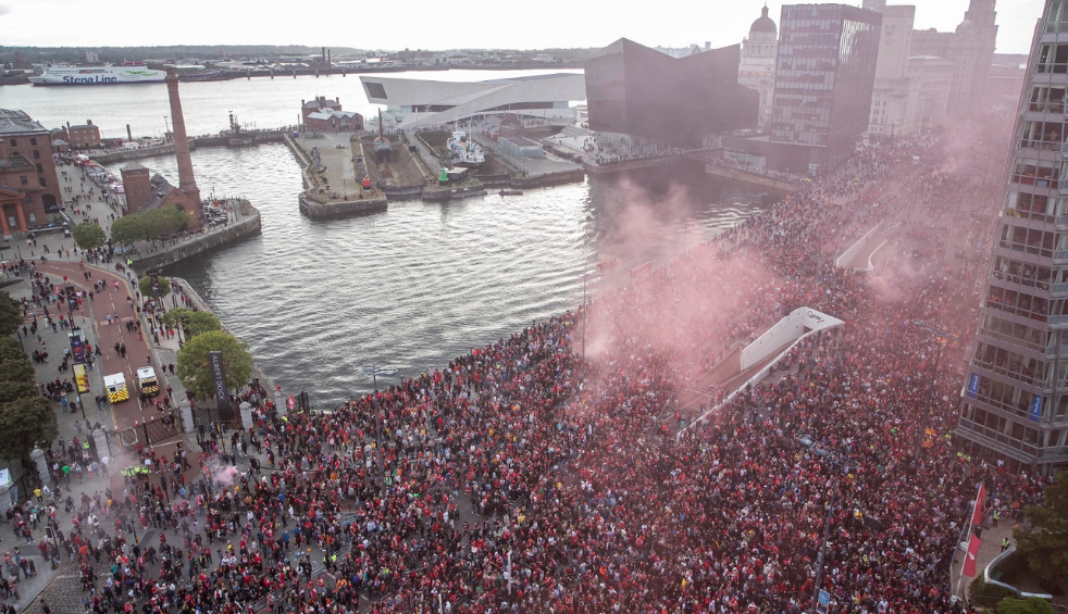 A large crowd of people on a road in Liverpool as a parade bus for the Liverpool FC parade goes through the crowd.