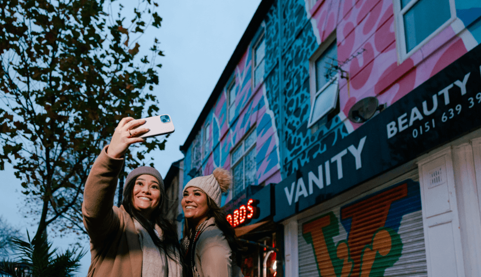 An image of two people taking a selfie style image with some street art behind them.