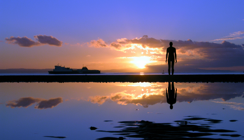 Croby Beach at sunset with one of the Antony Gromley statues and a ship sailing past.