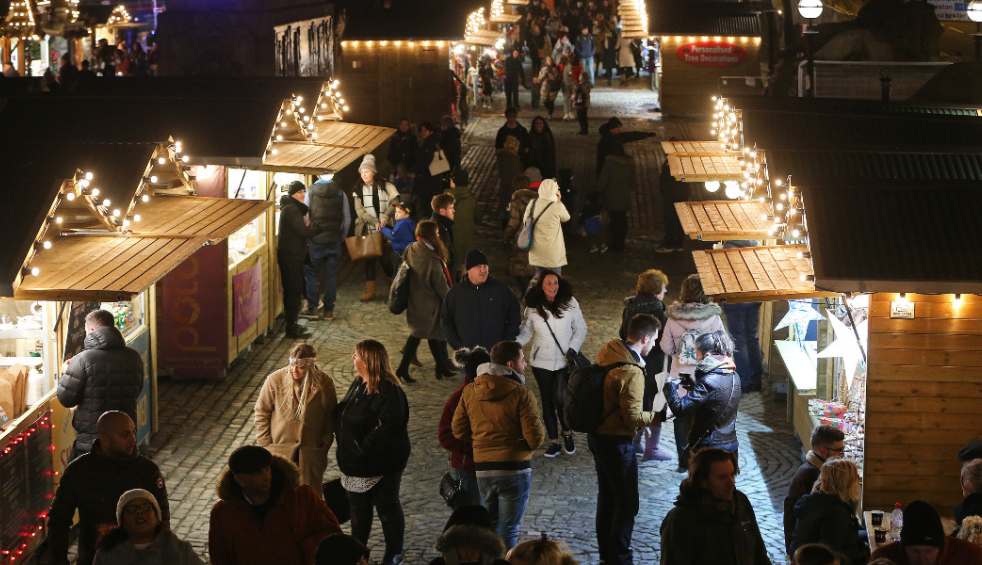 People strolling past Christmas market stalls at a festival/market.