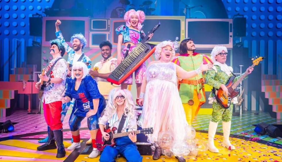 A cast from a panto show dressedin bright costumes on a stage with instruments.