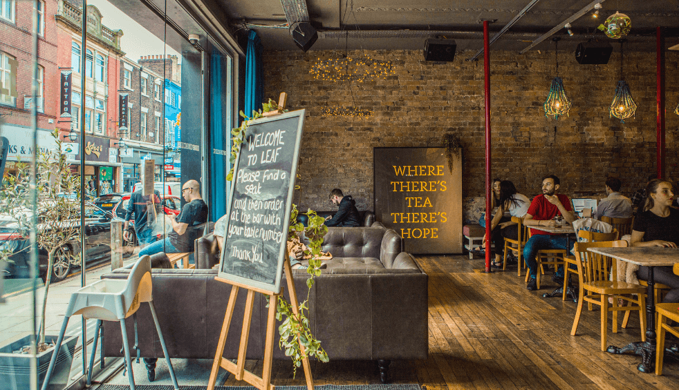 LEAF Liverpool dining area with people sitting waiting on food. The main wall is bricked with a large sign on the back wall saying 'Where there's tea there's hope'.