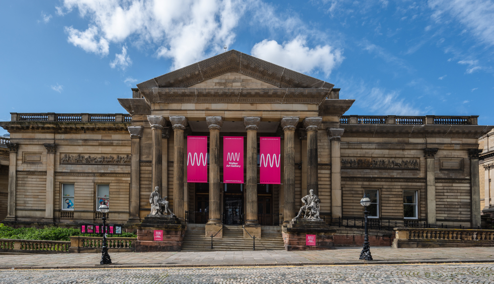 A large building made of stone with pillars around the entrance. There are pink banners hanging from the pillars.