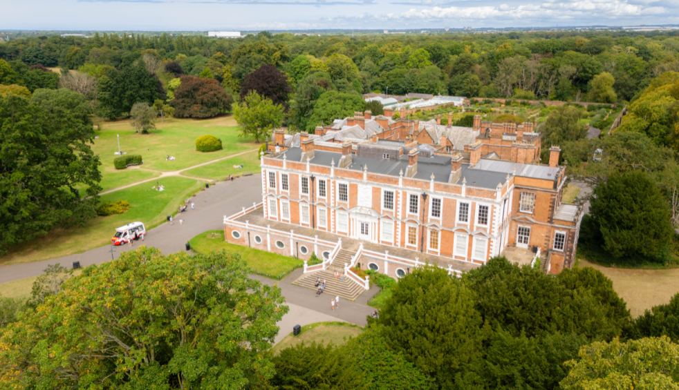 A drone shot of Croxteth Hall a large stately home surrounded by grass and trees.
