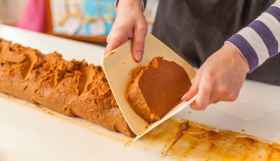 A long role of fudge with someone slicing it into chunks.