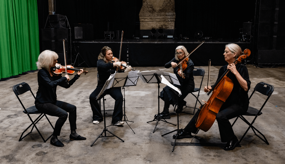 Four people playing string instruments in a warehouse