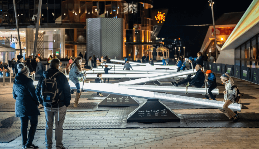 A light installation that is a line of see saws and people playing on them.