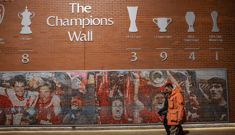 Two people walking past the champions league wall at Anfield.