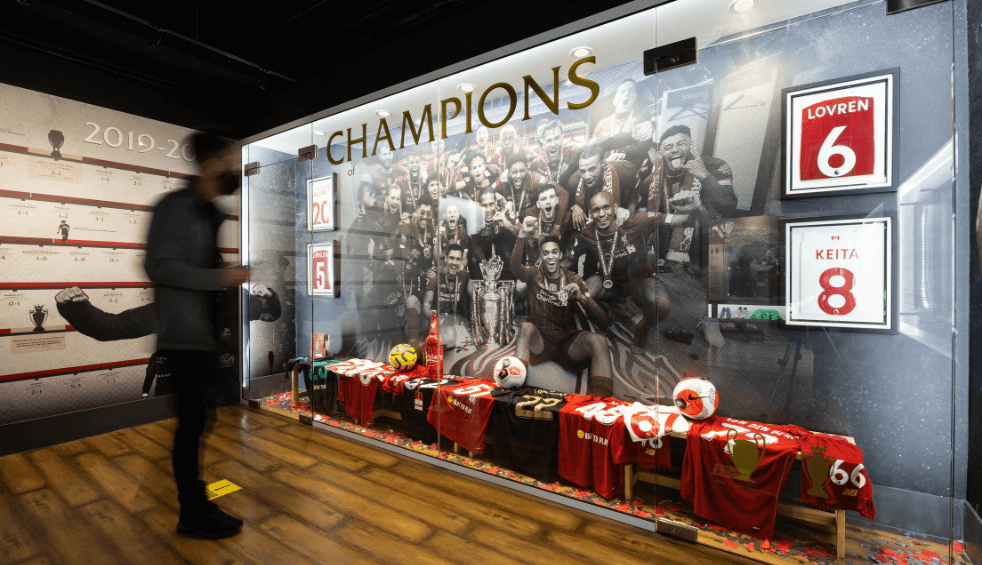 A person looking at a glass cabinet with LFC shirts and items in it.