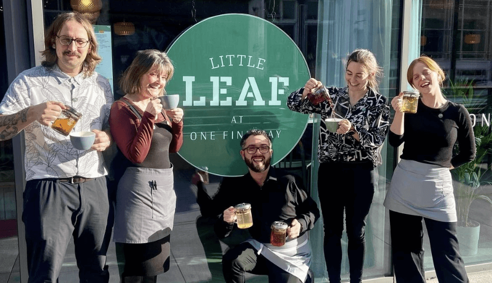 five people stood outside a glass window with Little Leaf signage on it.