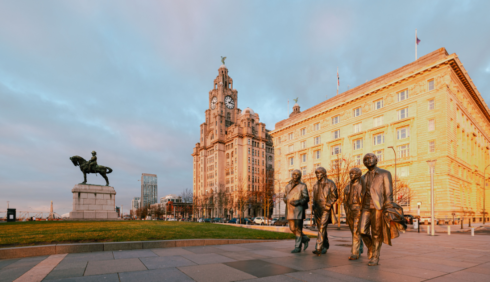The Beatles statue with the Royal Liver building in the background, with the sun setting on the Cunard building.