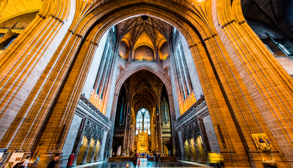 The interior of Liverpool Cathedral with a large stain glass window at the front and centre.