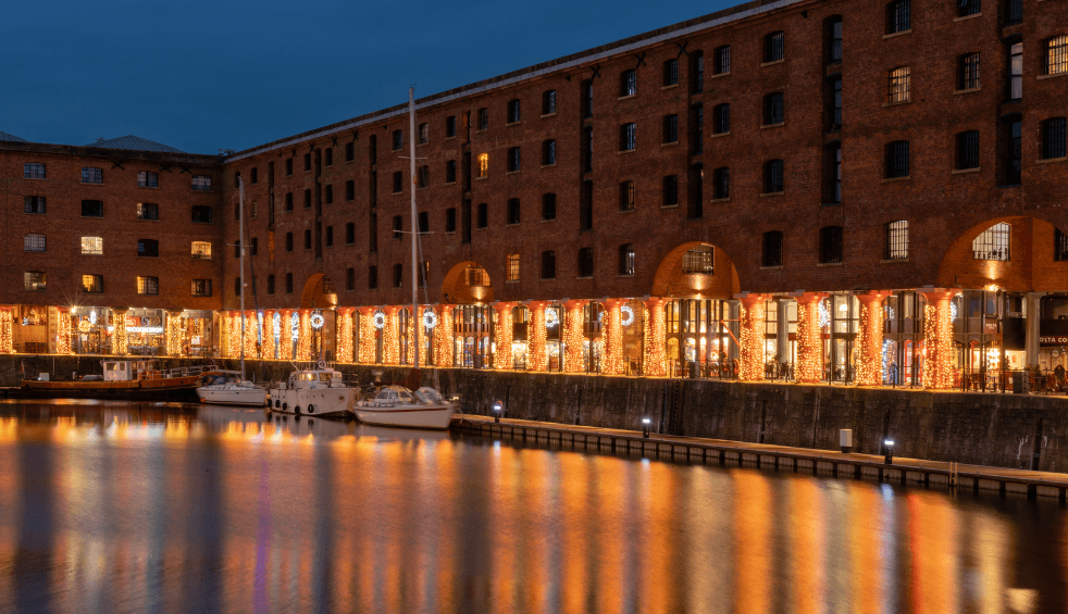 An image of the Royal Albert Dock at night, with each bollard light up in fairy lights.