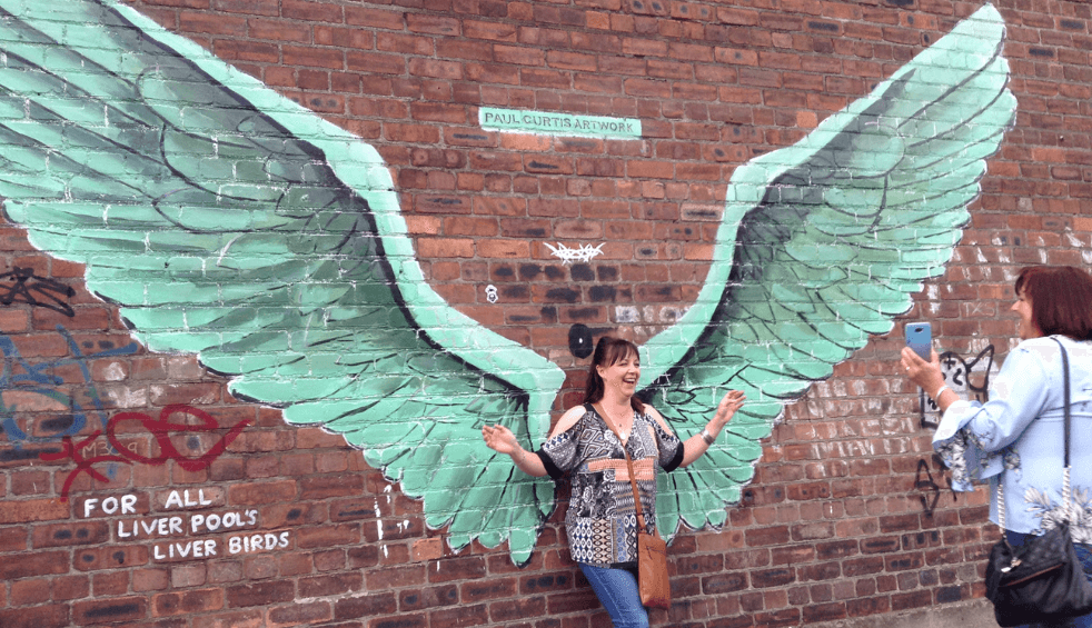 Paul Curtis Wings artwork on a wall with a person standing getting a photo with them.