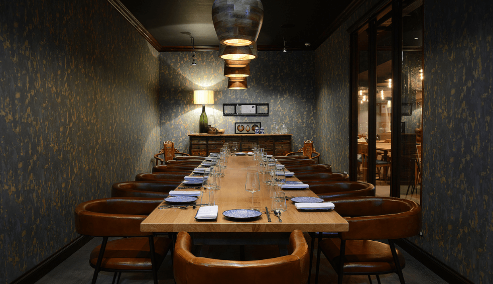 A long table set for 12 people in a room that is dimly lit. there are plates set at each seat.