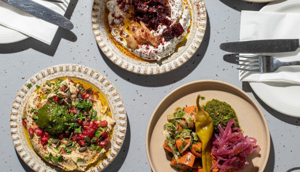 Three plates with food on it including hummus, a white dip and some salad.