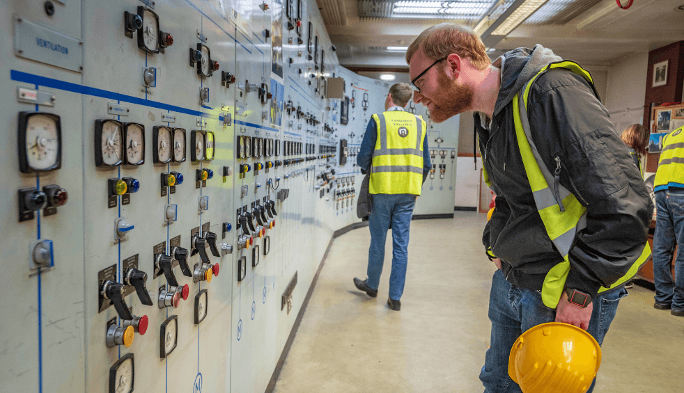 A person wearing a high vis yellow jacket looking at a control panel.