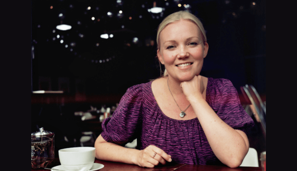 A person wearing a purple top sitting at a table with a cup of tea.