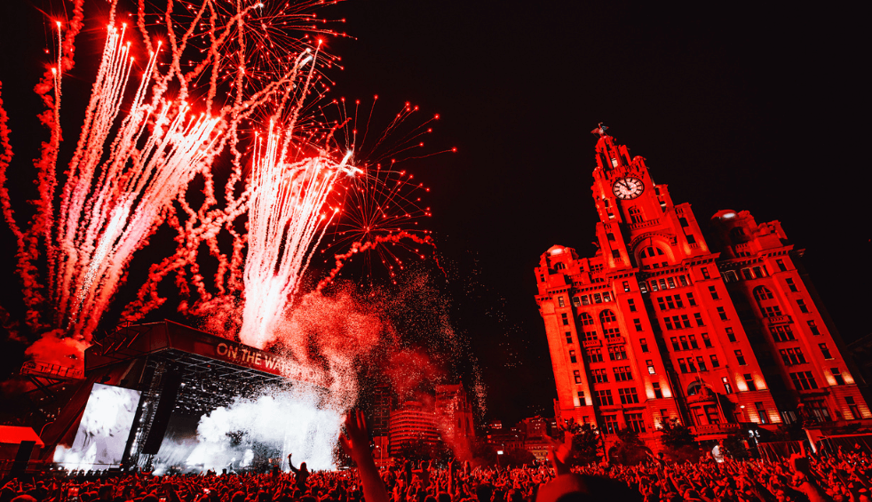 a festival site on Liverpool Pier head with a large stage with fireworks coming from the top of the stage.