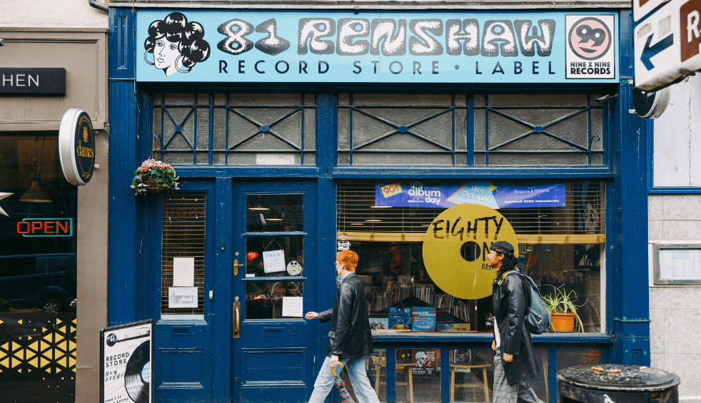 Two people walking in front of a record store which is blue.