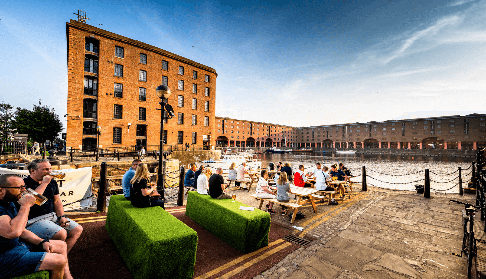 The Royal Albert Dock with people sitting outside at a bar.
