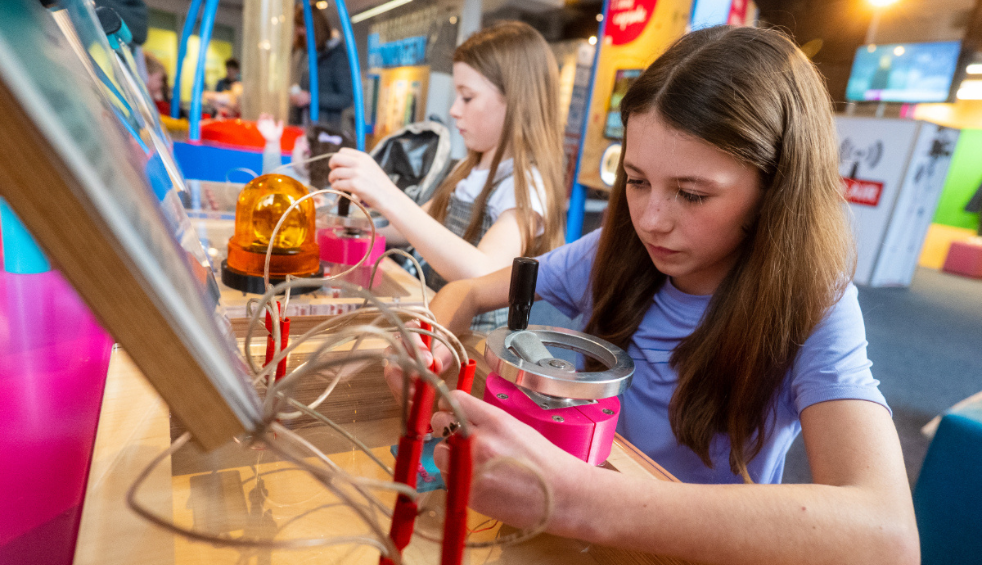 A young girl sitting playing with a science instrument.