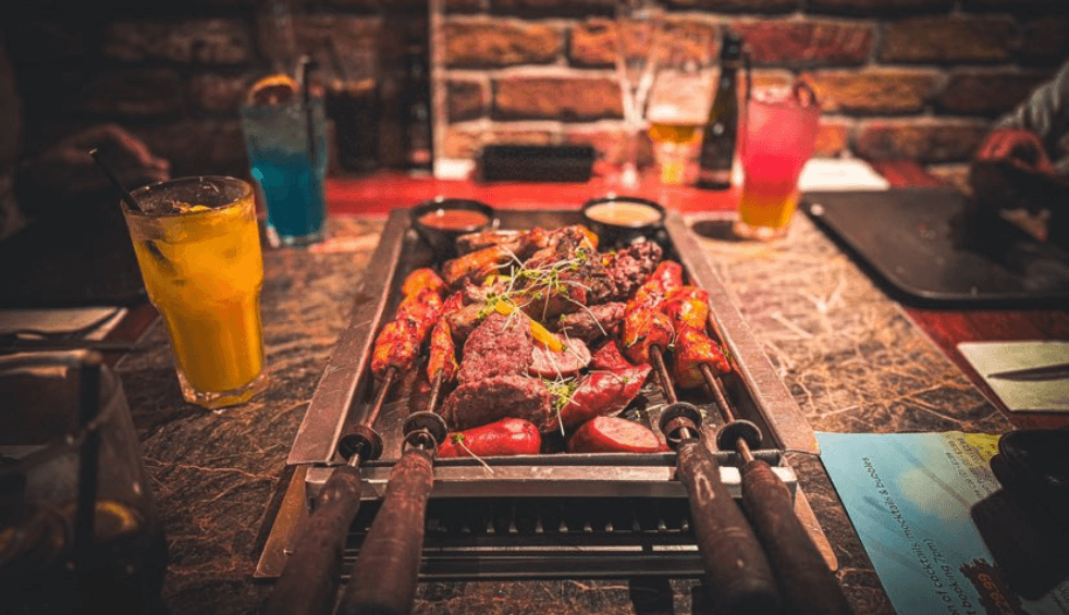 A table with a table top BBQ with meat on the grill.