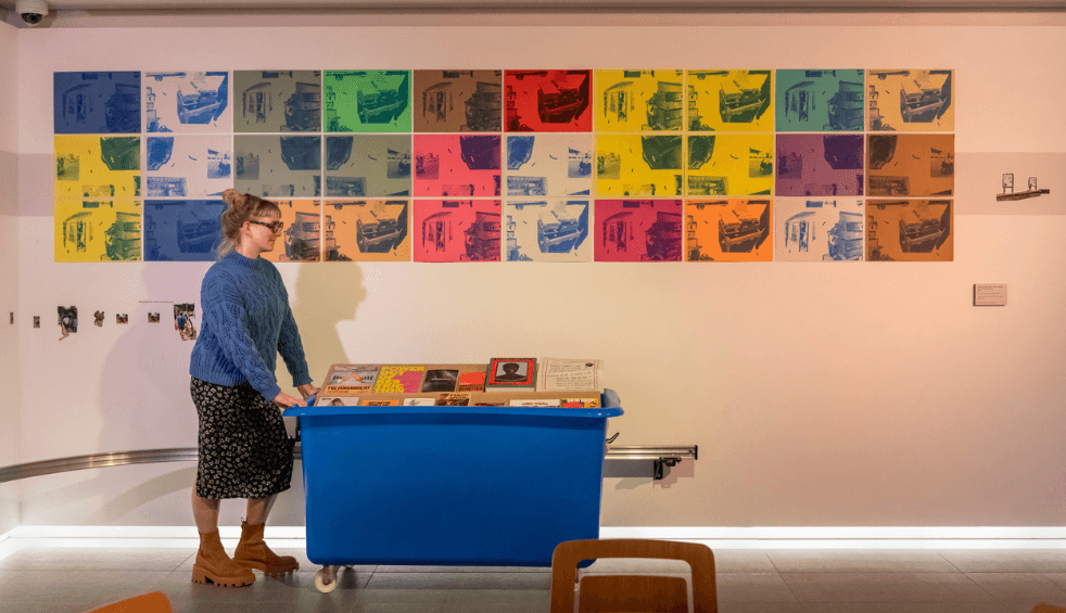 A person in Tate Liverpool next to an exhibition with photos on the wall.