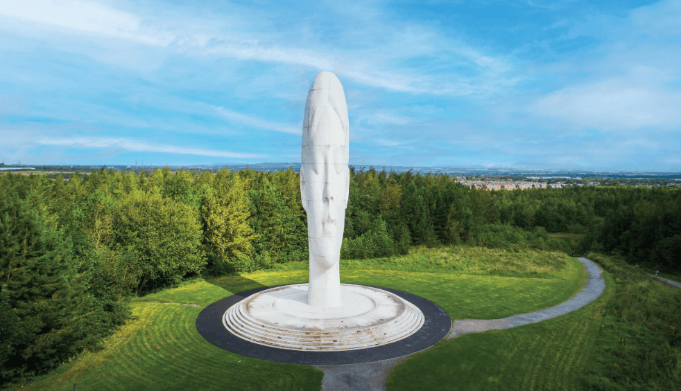 A large sculpture of a head made out of white stone in the middle of a grass land.