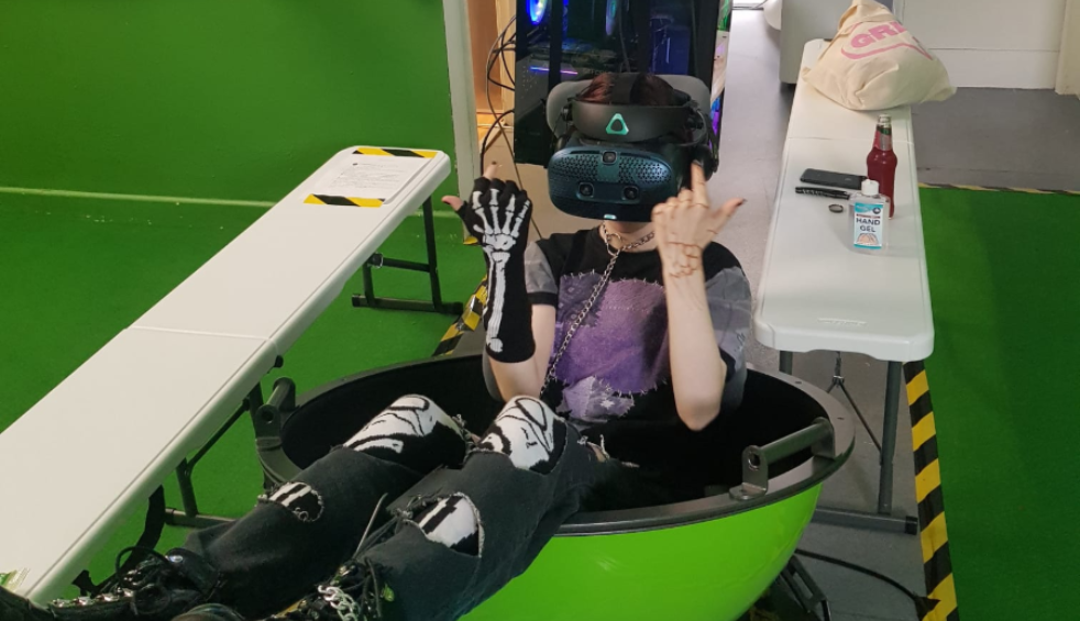 A person trying on a VR headset while sitting in a green semi circle chair.