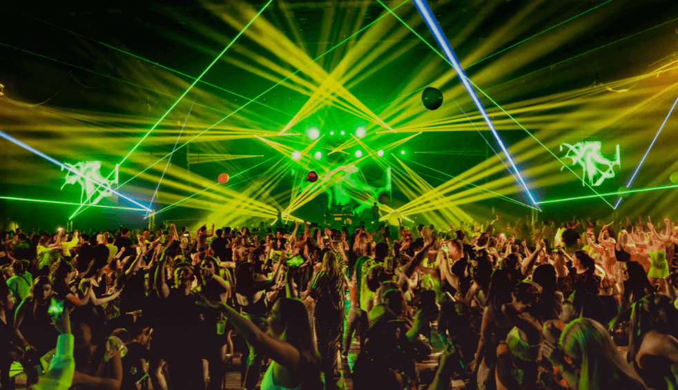 A huge crowd of people inside a warehouse with lots of green lasers