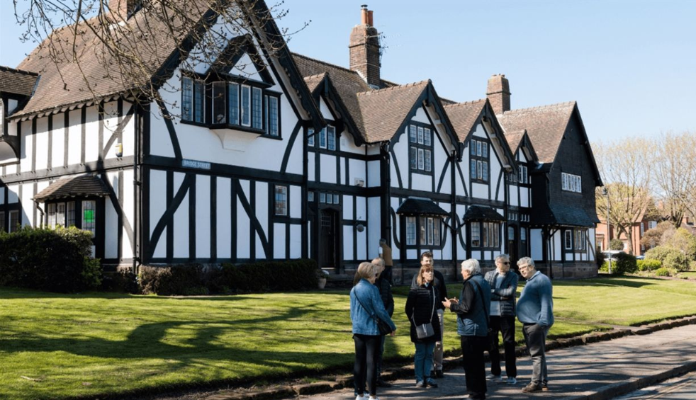 A group stands outside a black and white Tudor style house in Port Sunlight.