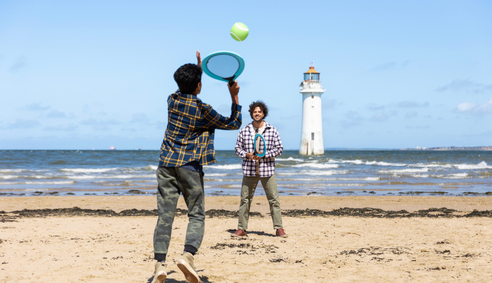 A father and son play tennis on New Brighton beach with New Brighton lighthouse in the background