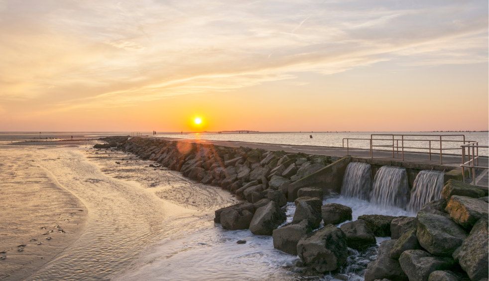 A stone walkway leading out to see with a sunset in the background.