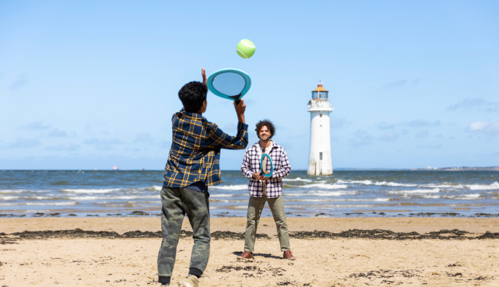 A family walk along the beach with New Brighton Lighthouse in the background