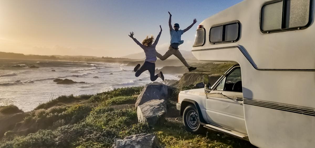 man and woman jumping in excitement next to their RV