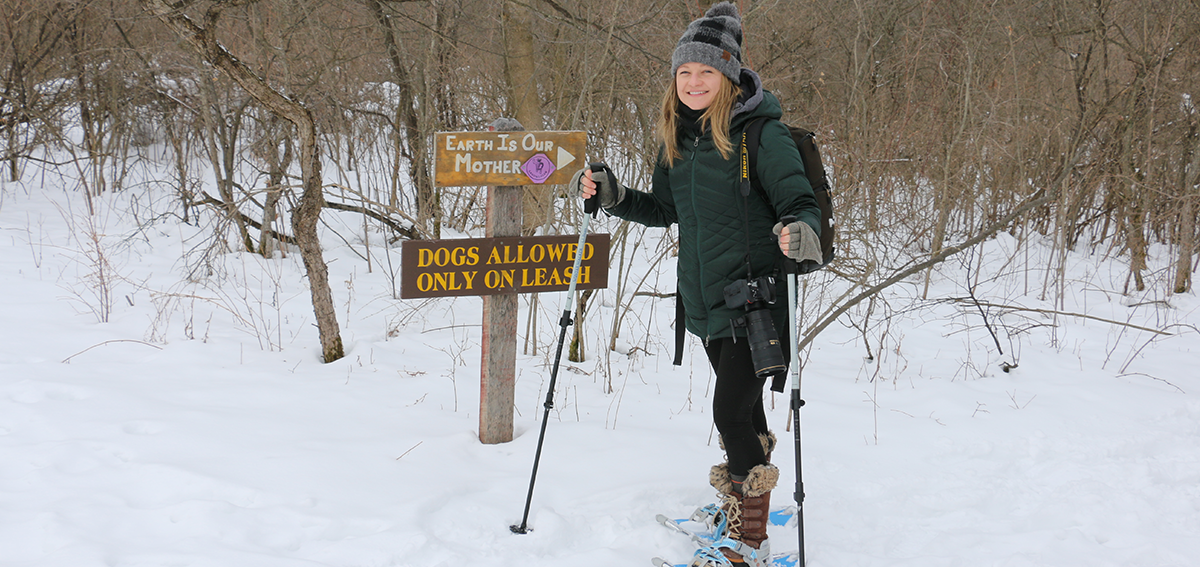 A snowshoer smiles on a trail at Ganondagan State Historic Site