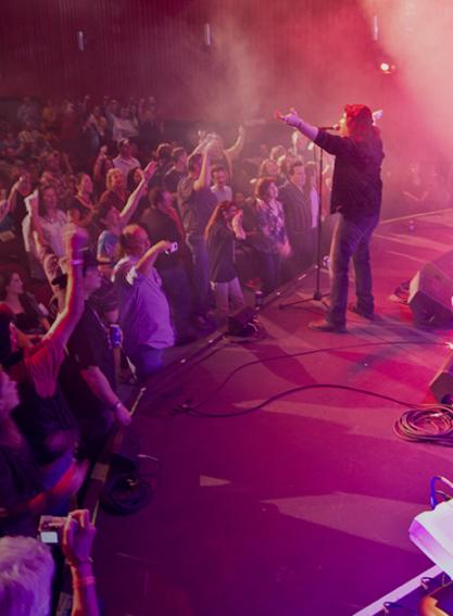 A band plays onstage to an excited crowd under blue and purple lighting at the Brauntex Theatre in New Braunfels, Texas.
