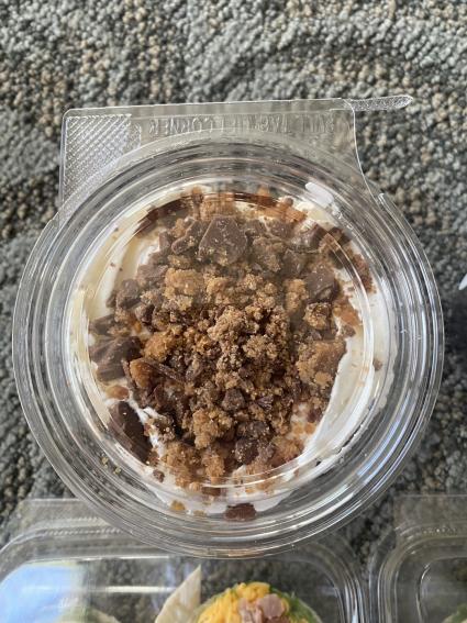 Crumbly topping on pudding in a closed clear container sitting on blue carpet