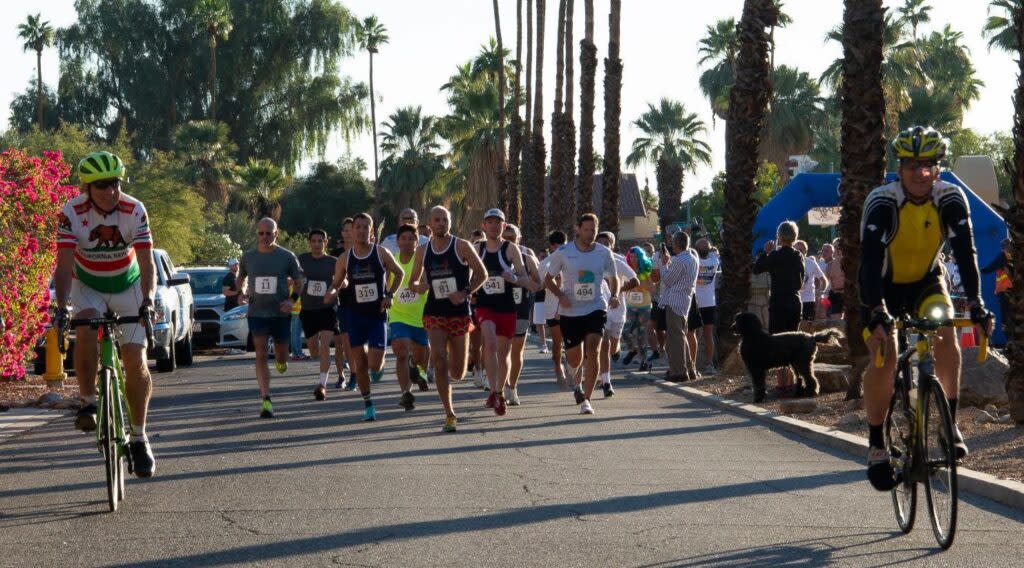 Runners and cyclists during an outdoor race event, with palm trees and spectators in the background.