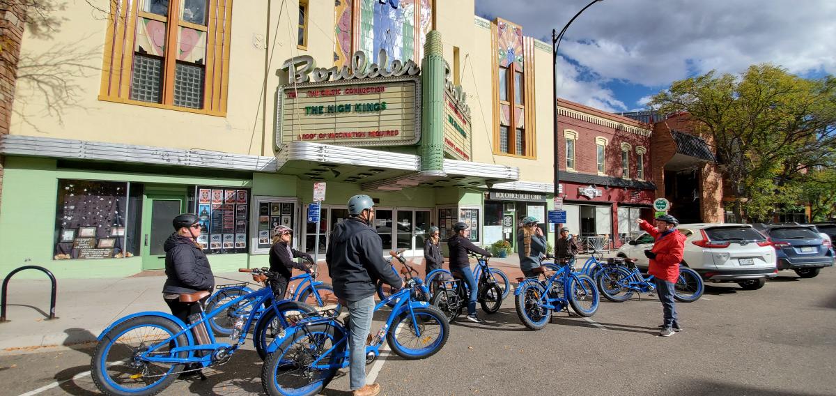 People listening to a tour guide on the Electric Bike Tour outside the Boulder Theater