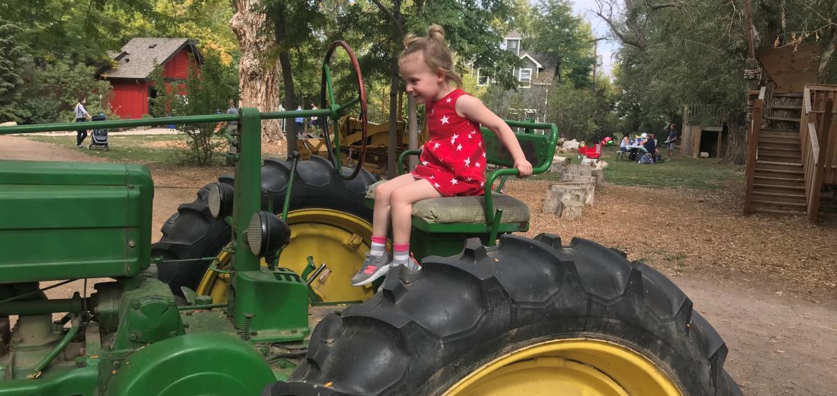 Little girl in a red sundress riding on a John Deer tractor at Sunflower Farm