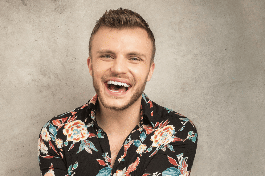 a headshot of a smiling Lee Peart sat against a wall