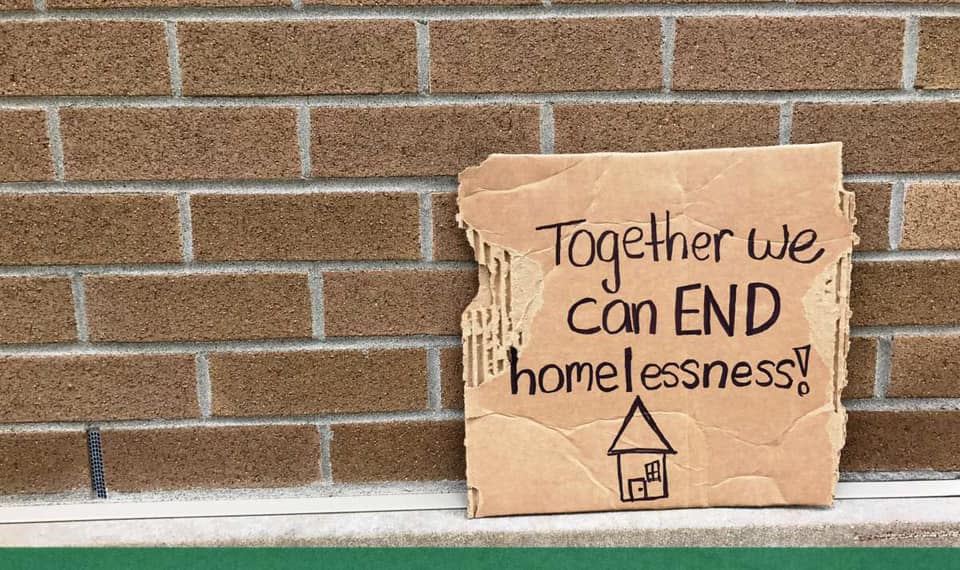 Cardboard sign that reads "together we can end homelessness!" against brick wall