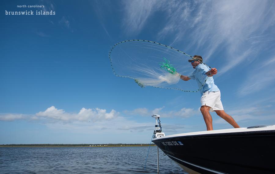 man standing on a boat throwing a net out into the ocean